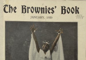 A young black girl smiles and poses, arms outstretched and standing on ballet pointe shoes. She wears a white dress, crown, and cape tied at her wrists.