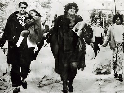 Evelina Antonetty and parents protest poor lunch quality at schools. One woman is carrying a child, walking across Federal Plaza in Manhattan and other parents carry large plastic bags of food.