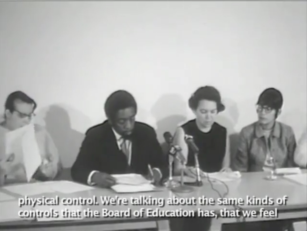 A panel of Black and Latinx parent advocates sit in front of microphones in a TV studio. Some parents read written remarks and some listen.